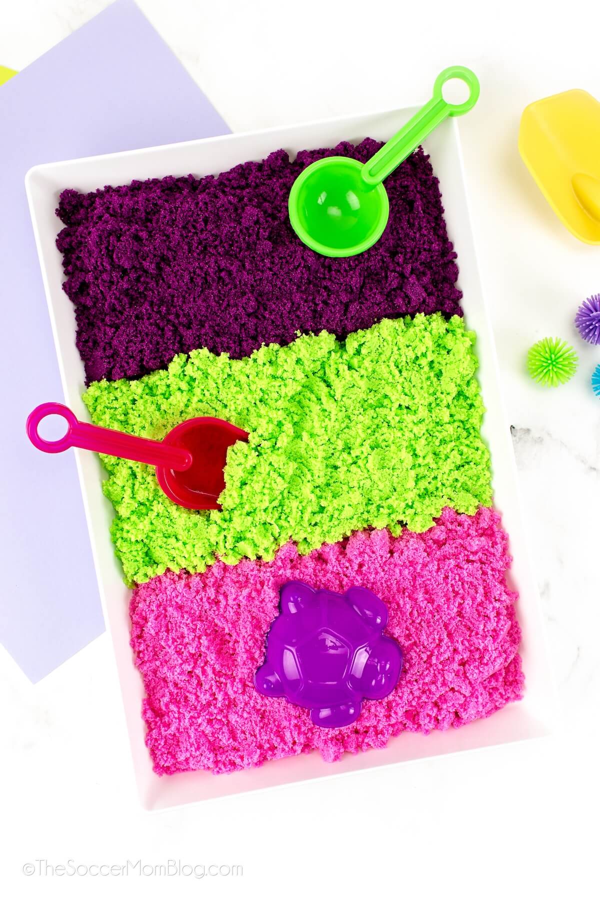 plastic play tray with 3 colors of homemade kinetic sand: purple, green, and pink