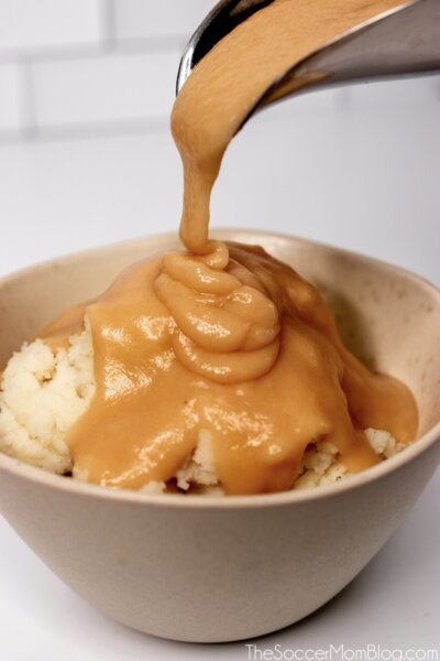 pouring brown gravy onto a bowl of mashed potatoes