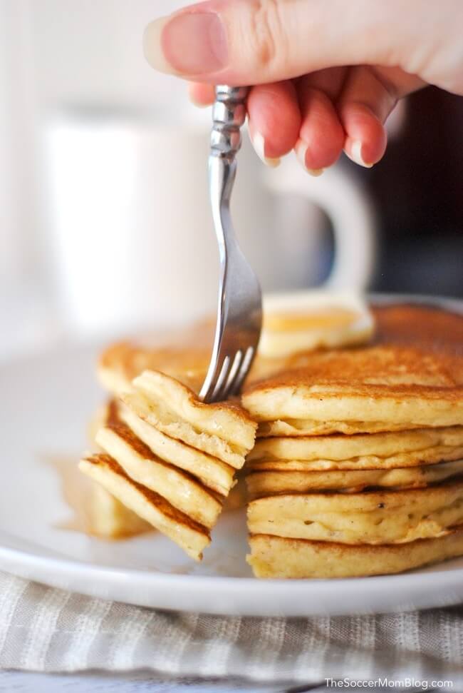 Cutting into a stack of fresh pancakes with coffee mug in background