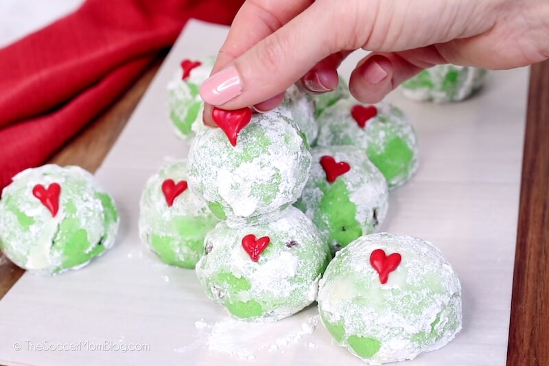 placing red heart decoration on Grinch snowball cookie