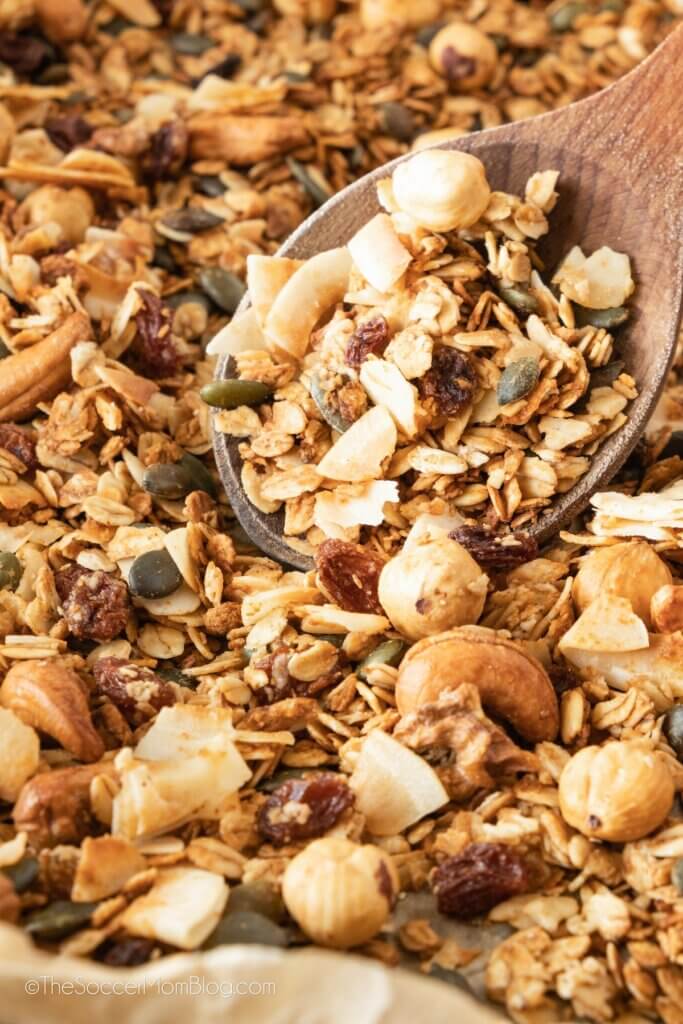 close up of homemade granola on baking sheet with wooden spoon