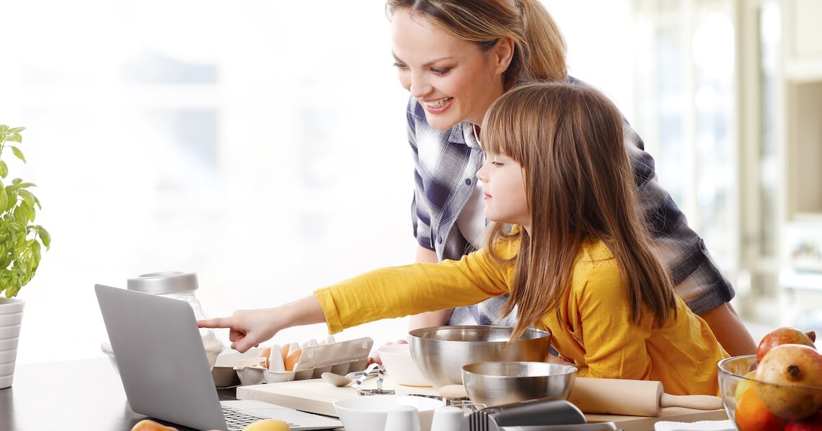 mom blogger with daughter on laptop working in kitchen